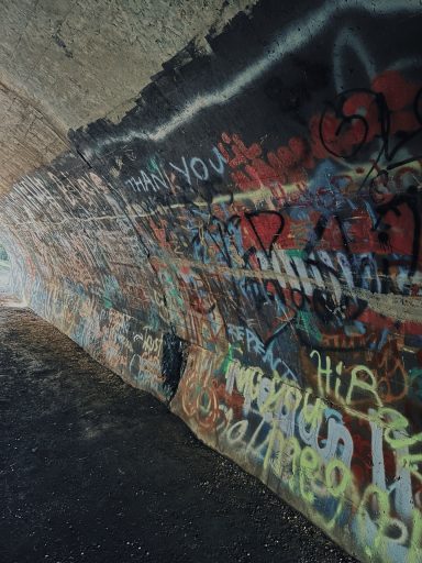 Colorful graffiti covers a curved wall inside a dimly lit tunnel.